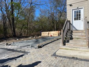 view of rear of 2-family home, with pavers surrounding a rectangular area of gravel and metal supports